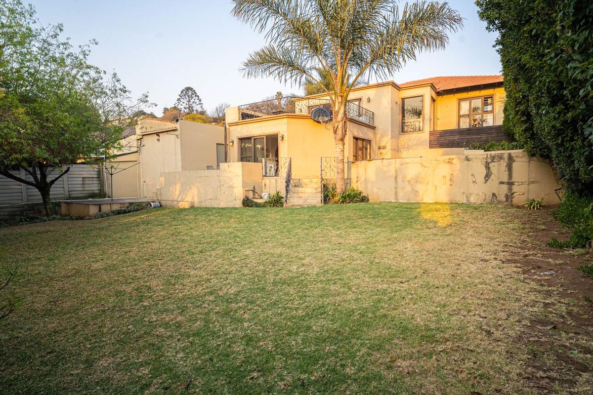 Rear view of the property featuring a spacious lawn, a raised patio area with wrought iron railings, and a multi-level exterior facade.