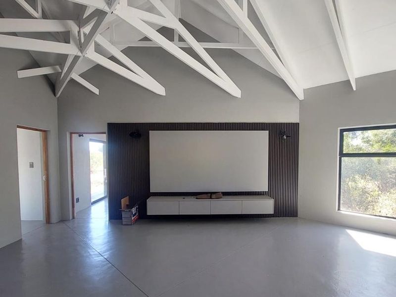 Spacious living area featuring a dramatic vaulted ceiling with exposed white trusses, polished concrete floors, and a modern slatted timber media feature wall.