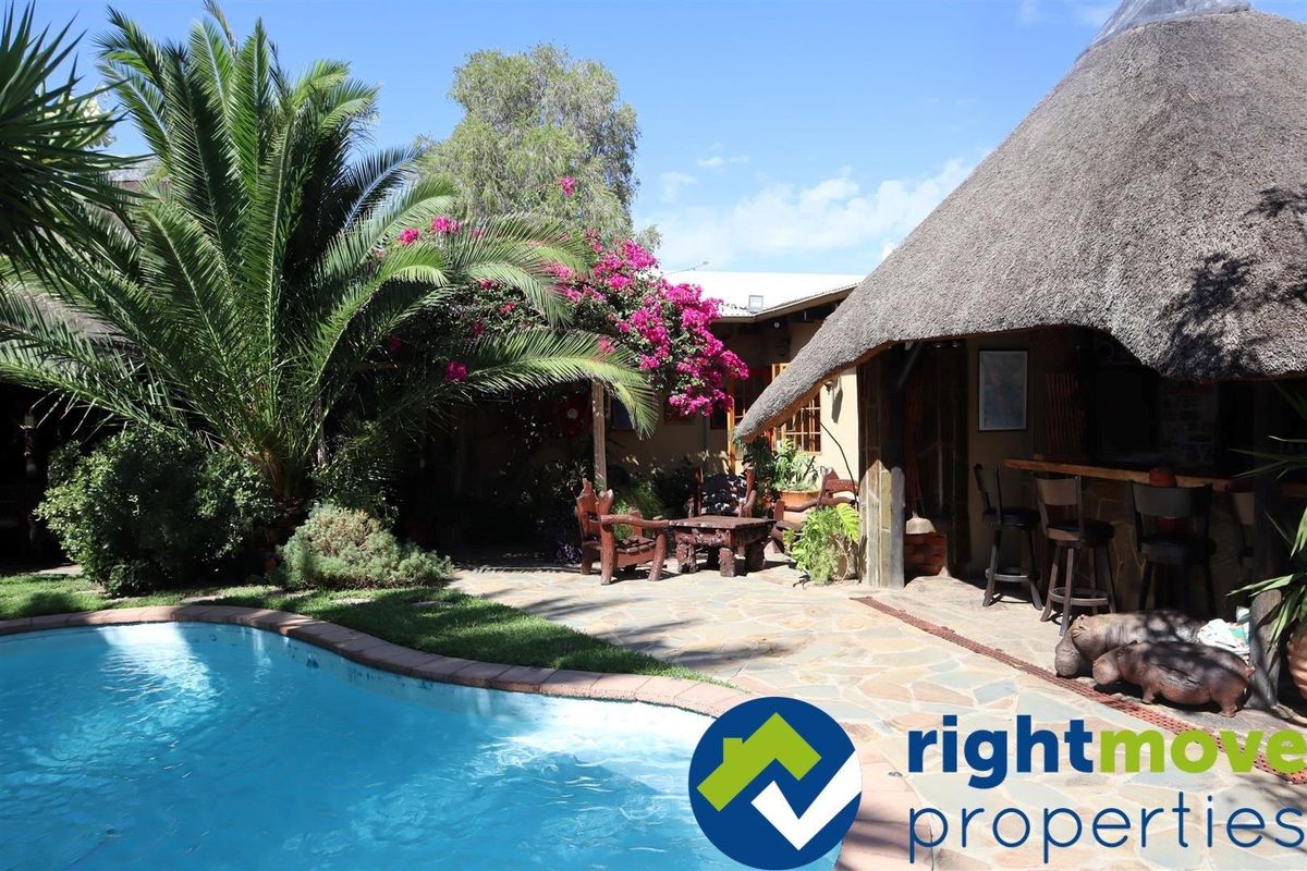 Outdoor pool area featuring a thatched roof entertainment space with a built-in bar and stone paved patio surrounded by established garden landscaping.