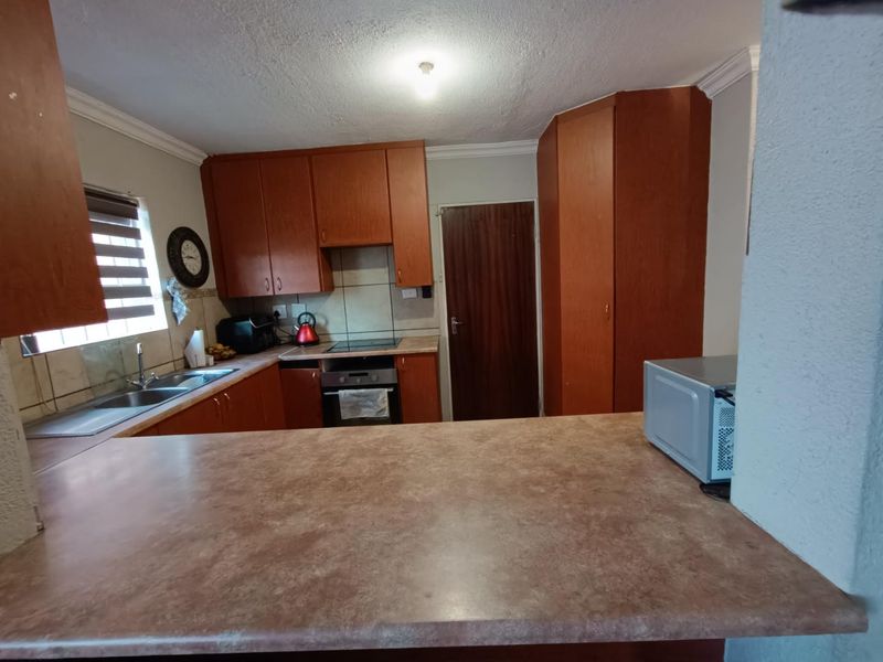 A functional kitchen featuring wood-tone cabinetry, laminate countertops, a breakfast bar, and integrated cooking appliances with a tiled backsplash.