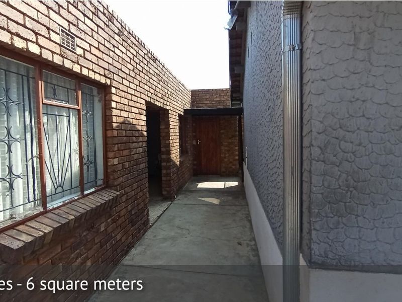 A narrow exterior side passage featuring face brick and textured render walls with a concrete walkway and metal downpipe.