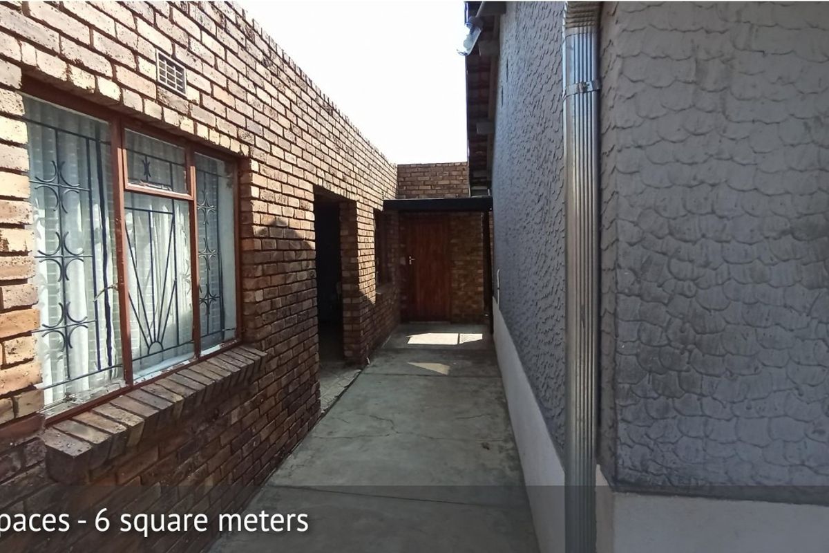 A narrow exterior side passage featuring face brick and textured render walls with a concrete walkway and metal downpipe.