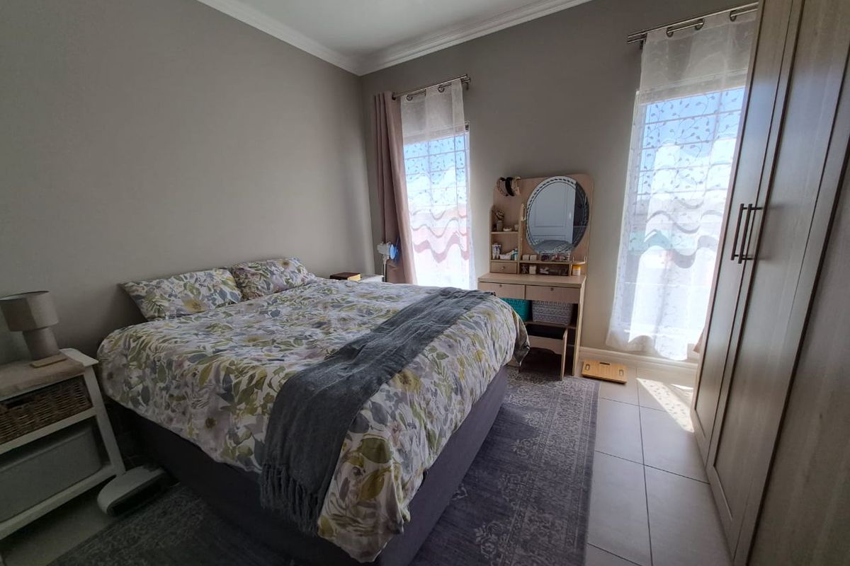 A well-lit bedroom featuring neutral wall tones, tiled flooring, decorative cornicing, and a spacious built-in wardrobe.