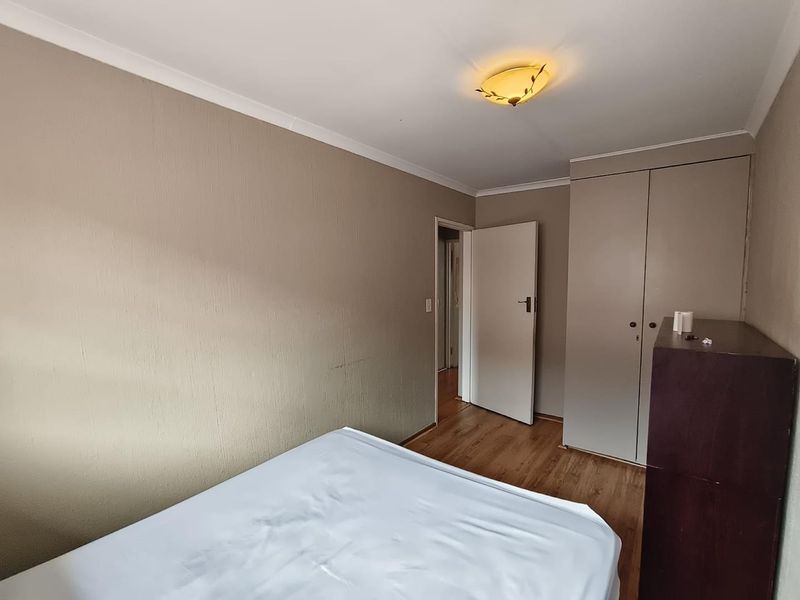 A bedroom featuring laminate flooring, built-in cupboards, and a neutral wall finish, providing a functional space with standard fixtures.