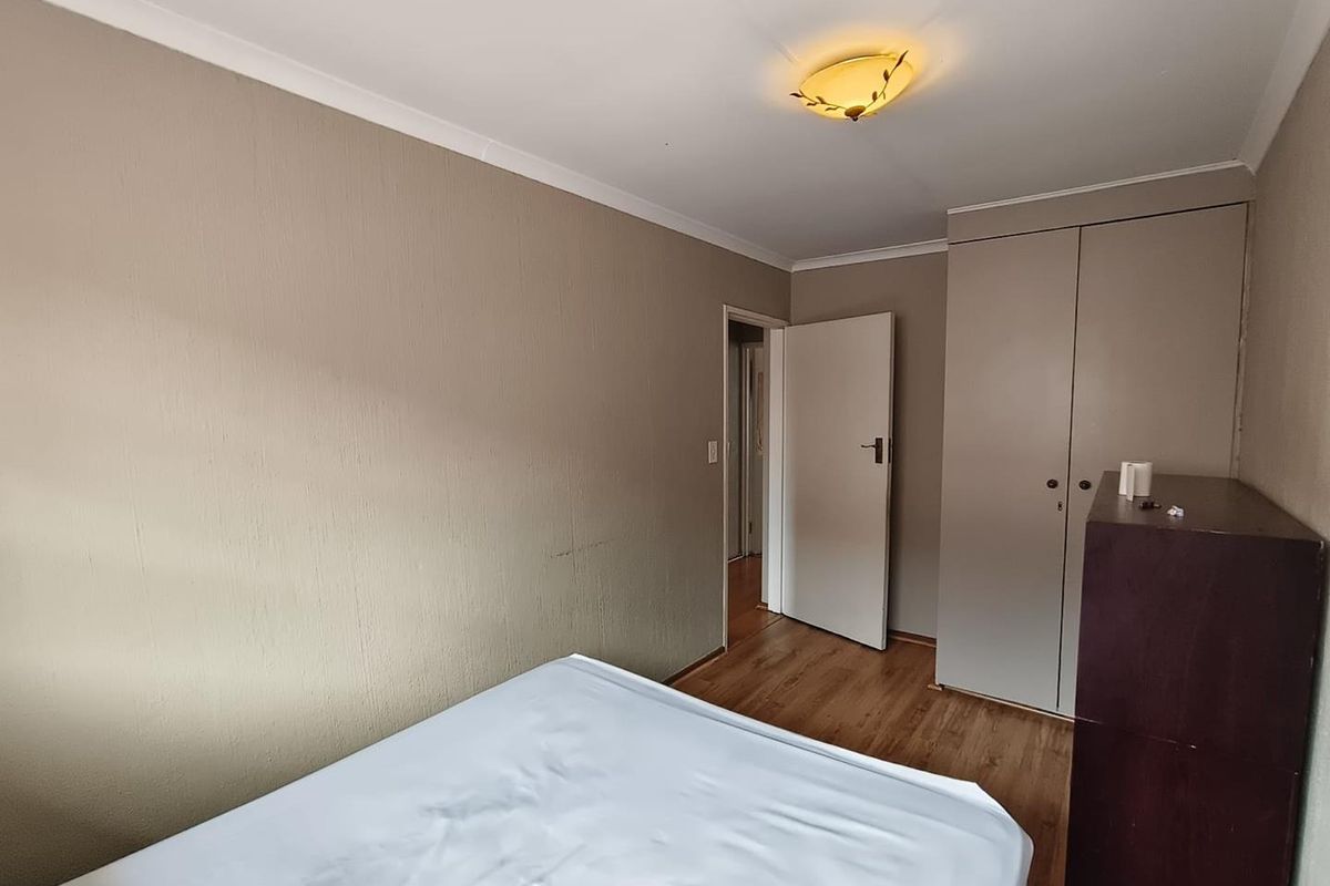 A bedroom featuring laminate flooring, built-in cupboards, and a neutral wall finish, providing a functional space with standard fixtures.