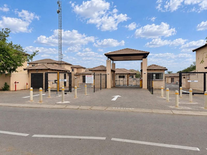 The secure entrance to the townhouse complex features a gated access point, paved driveway, and dedicated visitor parking area.