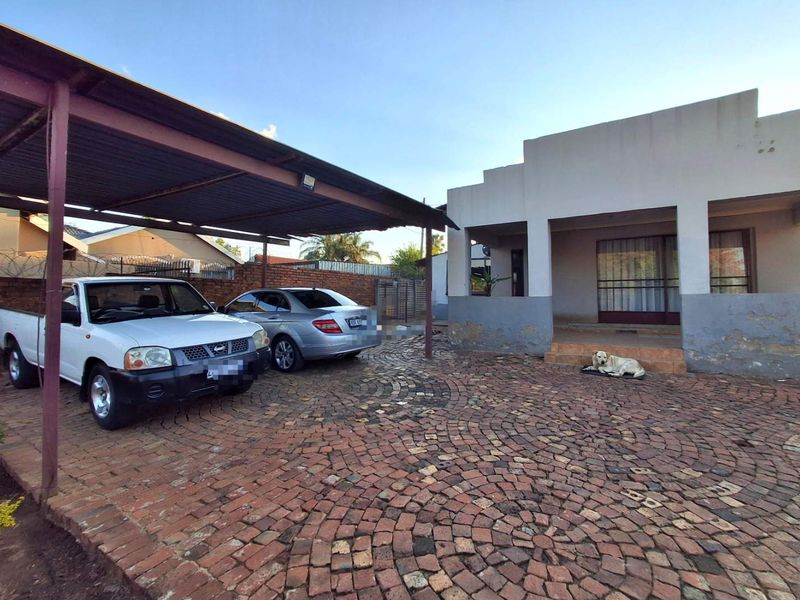 Front exterior view of the house featuring a paved cobblestone driveway, a metal carport structure, and a covered entrance porch.