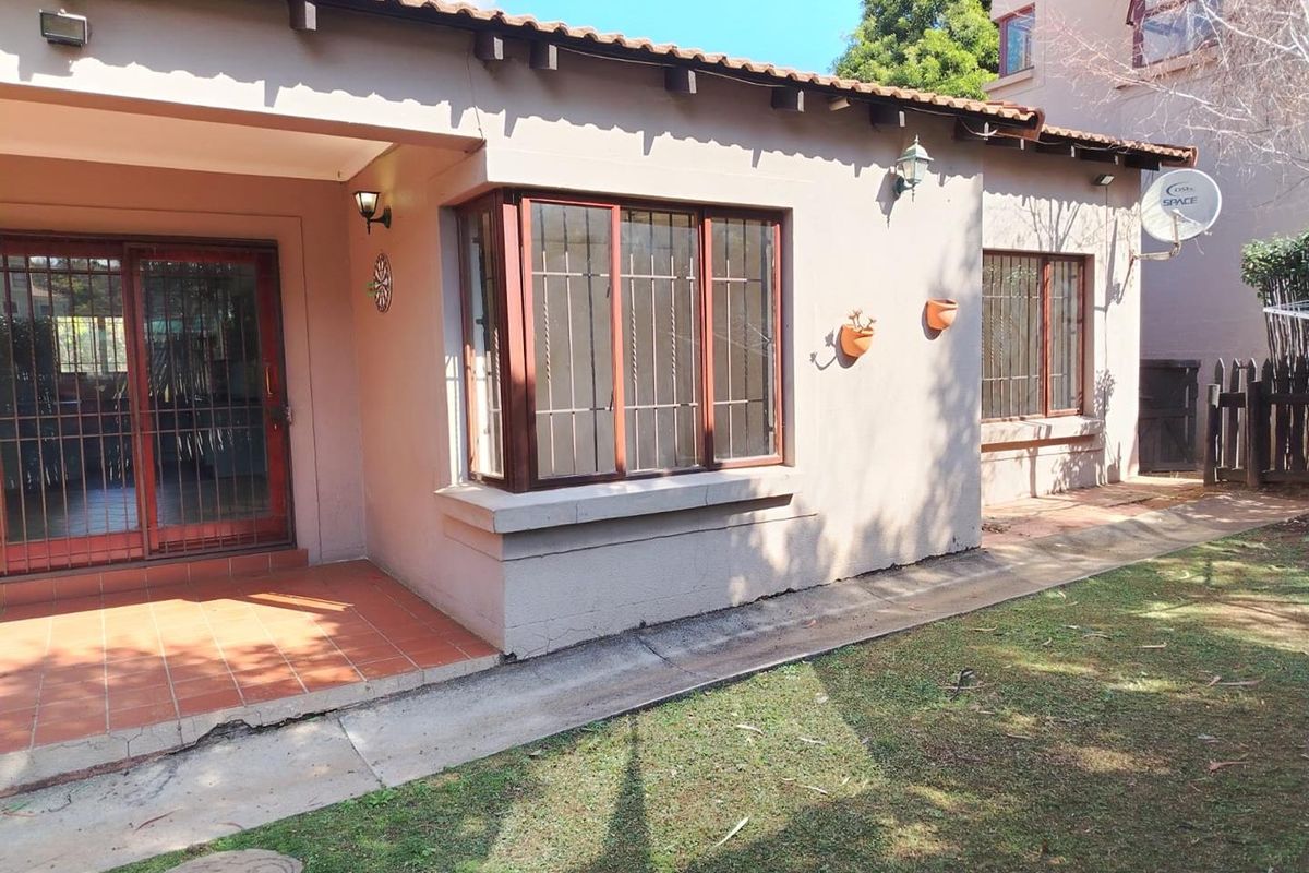 Rear view of the townhouse featuring a tiled patio, sliding glass doors, bay window, and a small garden area with paved walkway.