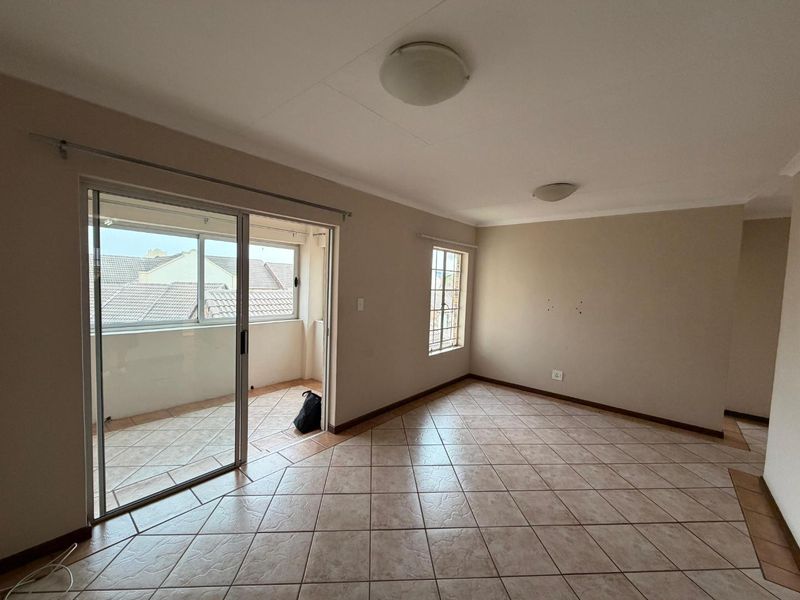 An empty living room featuring tiled flooring, neutral walls, and a sliding glass door providing access to a balcony.
