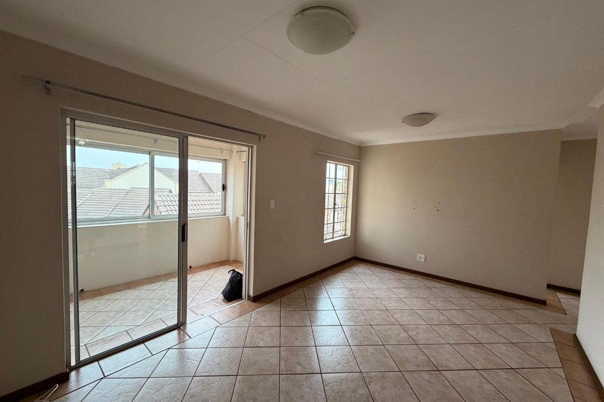 An empty living room featuring tiled flooring, neutral walls, and a sliding glass door providing access to a balcony.