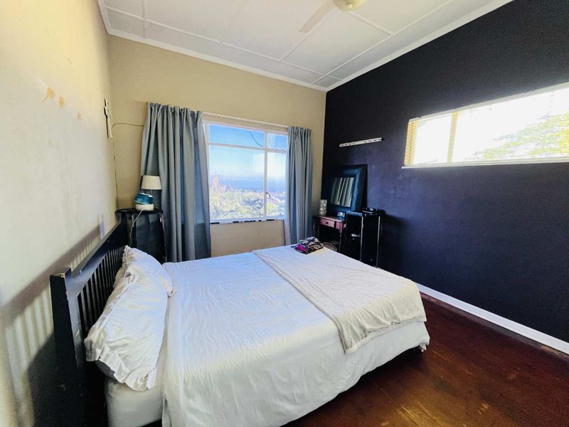 A bedroom featuring dark accent wall, timber flooring, and large windows providing natural light and views.
