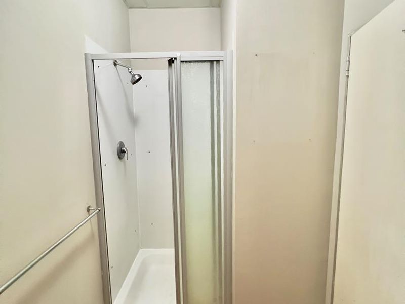 A compact bathroom featuring a standalone shower cubicle with a glass door, laminate flooring, and a wall-mounted towel rail.