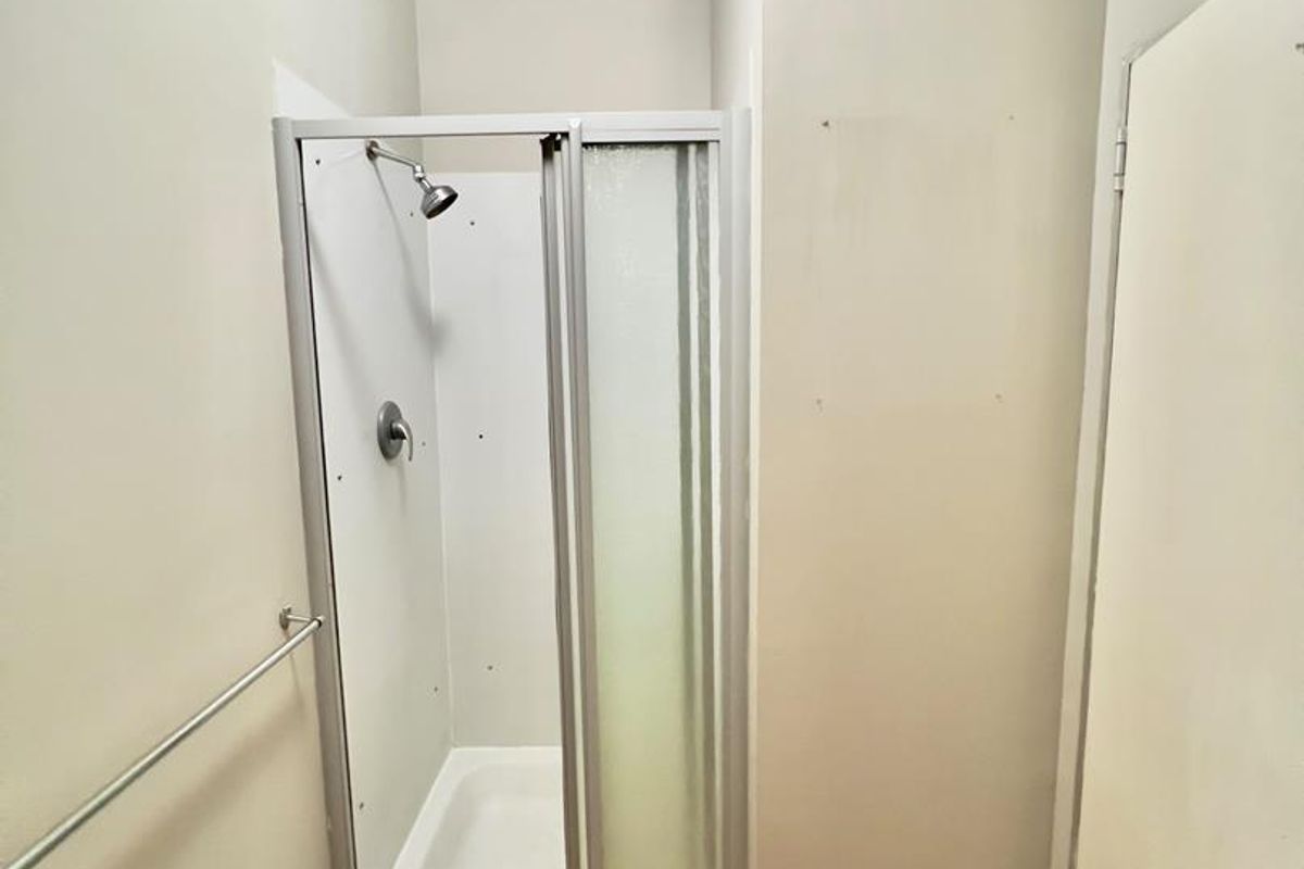 A compact bathroom featuring a standalone shower cubicle with a glass door, laminate flooring, and a wall-mounted towel rail.