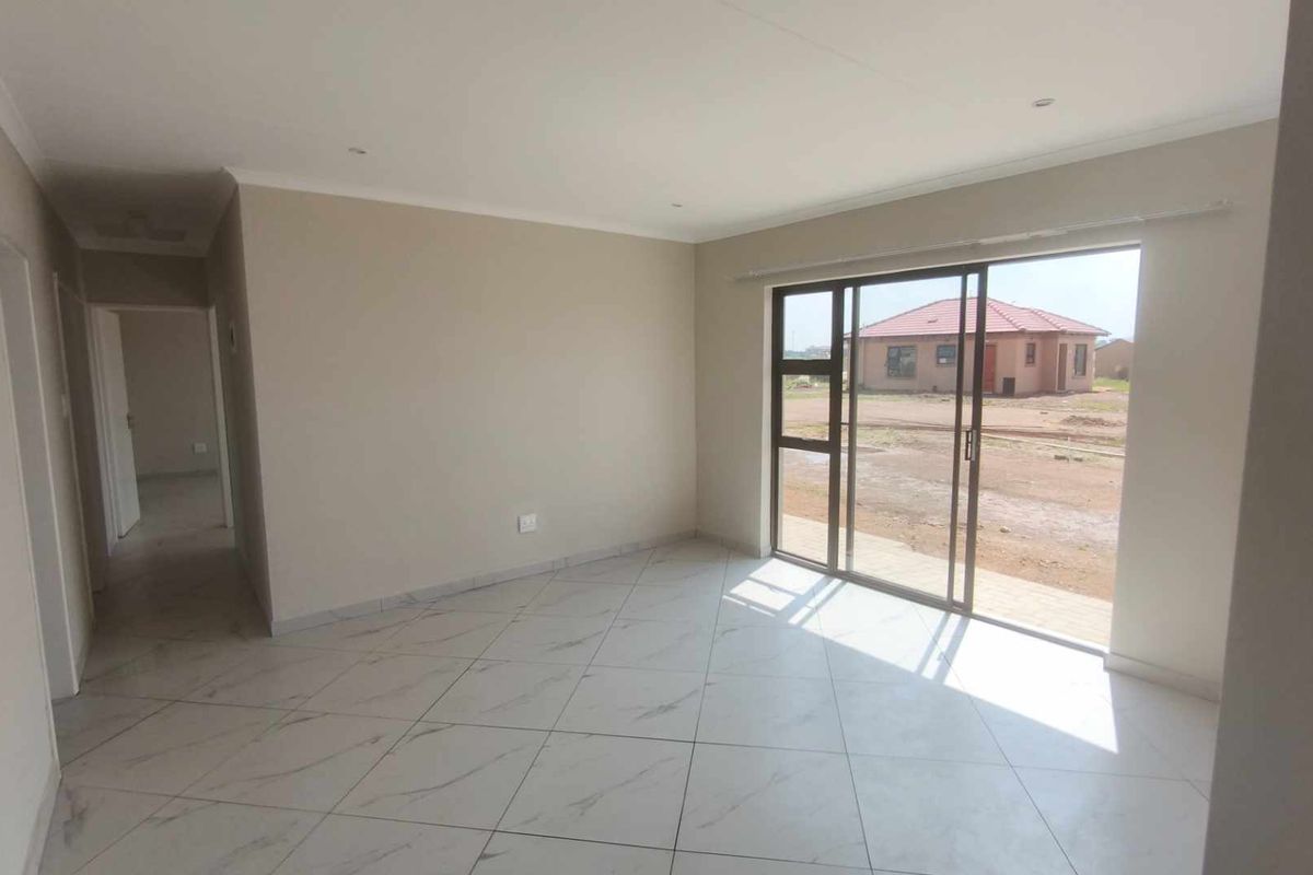 A bright, empty living area featuring neutral wall tones, modern tiled flooring, and large sliding glass doors providing access to the exterior.