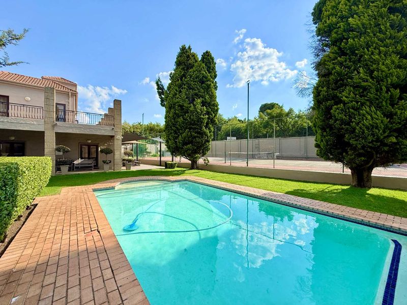 A well-maintained outdoor area featuring a swimming pool, brick paved surround, landscaped garden, and access to a private tennis court.