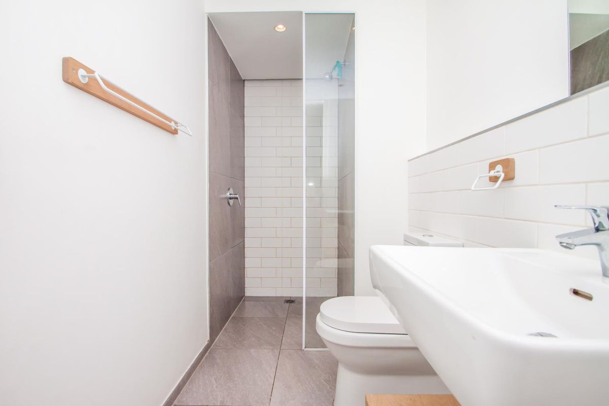 Modern bathroom featuring a walk-in shower with glass screen, white subway tiling, grey floor tiles, and a wall-mounted basin.