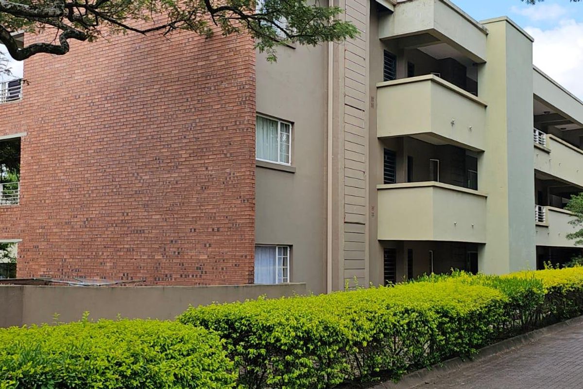 A multi-story apartment building featuring a combination of brick and painted concrete facades with private balconies and a paved driveway entrance.
