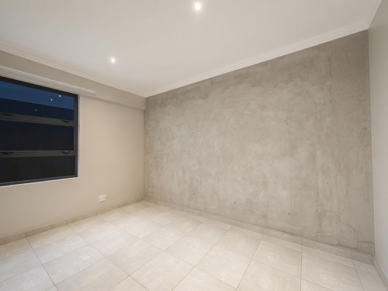 A bright, empty bedroom featuring modern tiled flooring, recessed downlighting, and a contemporary concrete feature wall.