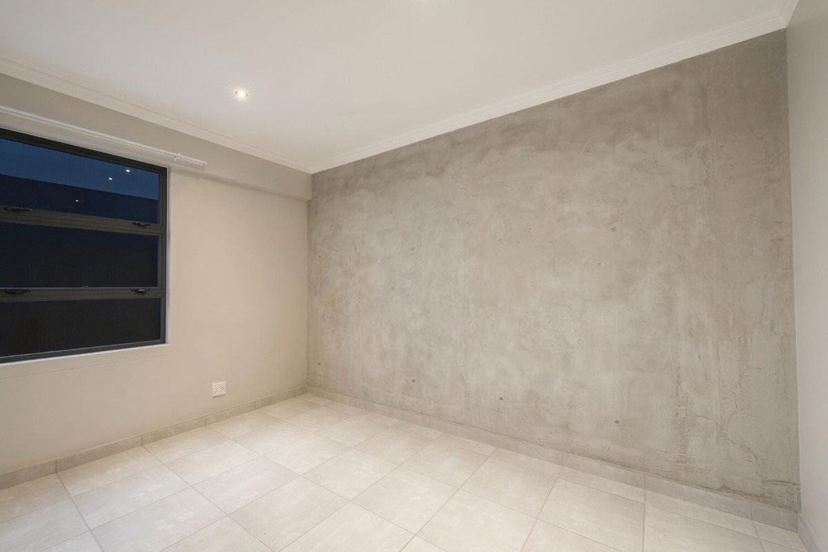 A bright, empty bedroom featuring modern tiled flooring, recessed downlighting, and a contemporary concrete feature wall.