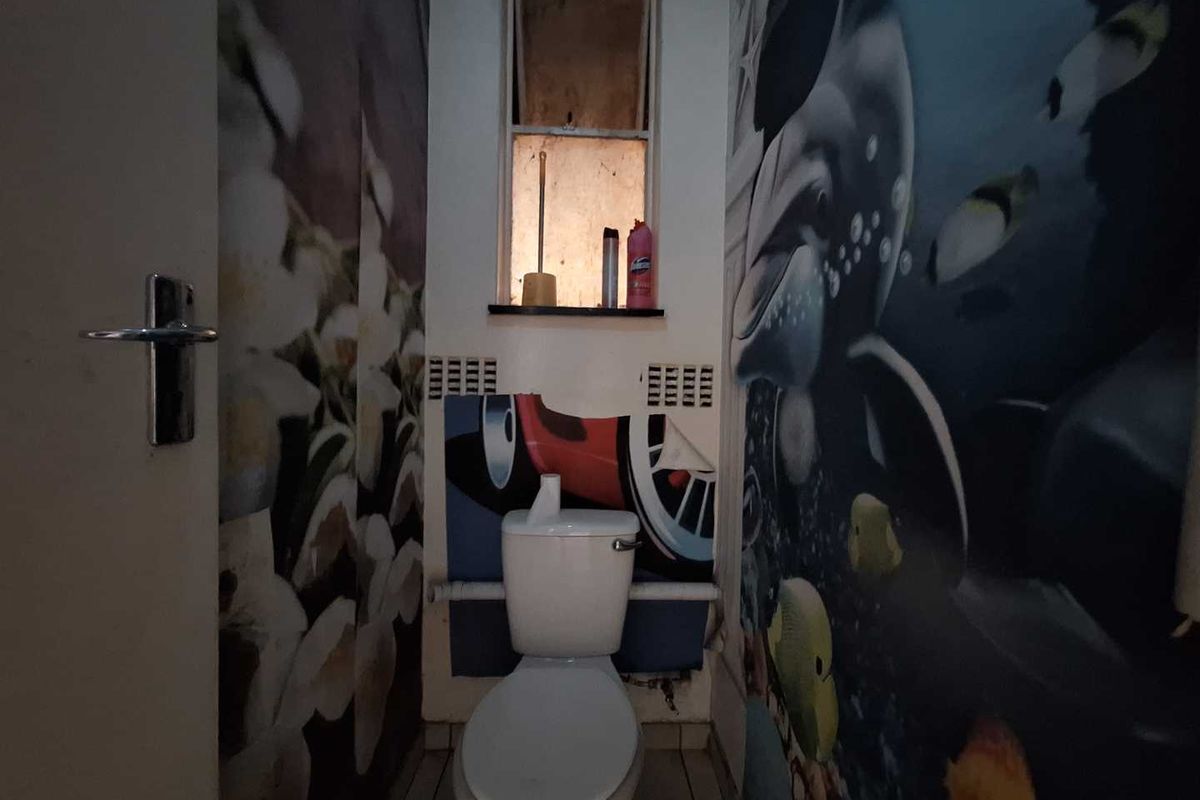 A small bathroom featuring a standard toilet, tiled flooring, and decorative wall murals in need of renovation.
