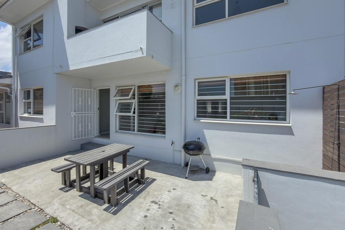 Rear exterior view of the apartment featuring a concrete patio area, security-fitted windows, and an overhead balcony.