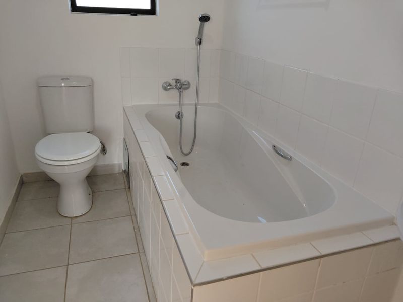 A functional bathroom featuring a standard bathtub with a shower mixer and a toilet, finished with white wall tiles and neutral floor tiles.