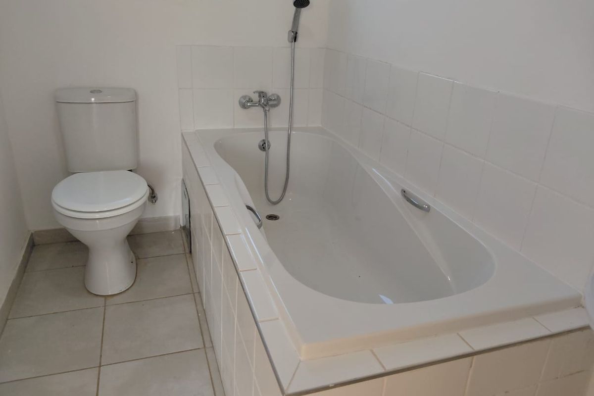 A functional bathroom featuring a standard bathtub with a shower mixer and a toilet, finished with white wall tiles and neutral floor tiles.