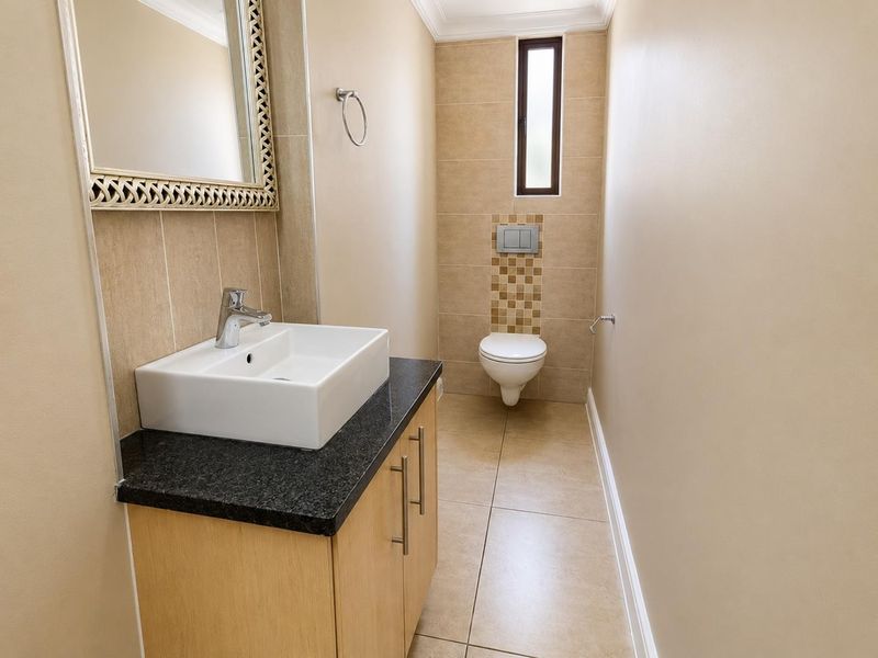 A modern guest bathroom featuring a wall-mounted toilet, a vanity cabinet with a granite countertop, and a vessel sink.