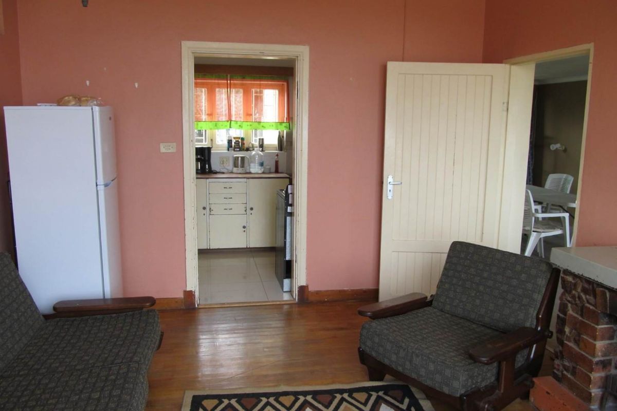 A living room featuring original timber flooring and a brick fireplace, with a doorway leading into a separate kitchen area.