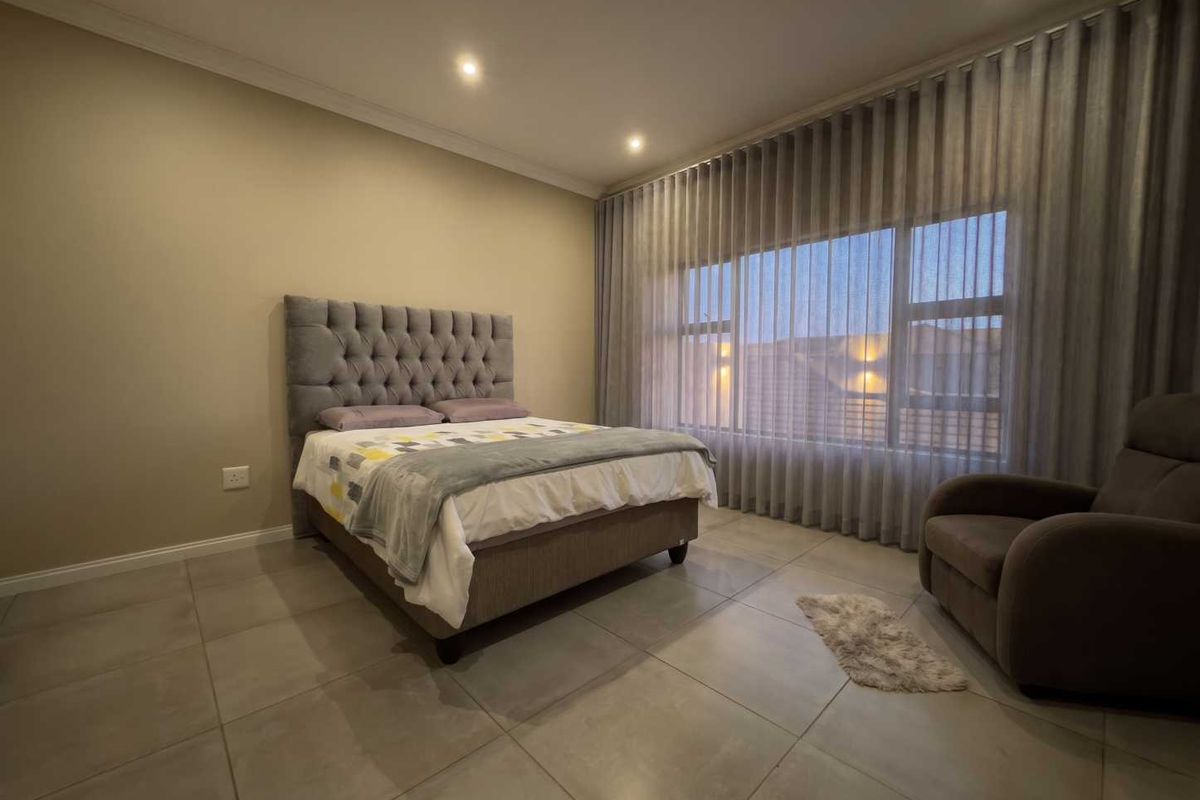 A well-maintained bedroom featuring large windows with floor-to-ceiling curtains, neutral tiled flooring, and recessed downlighting.
