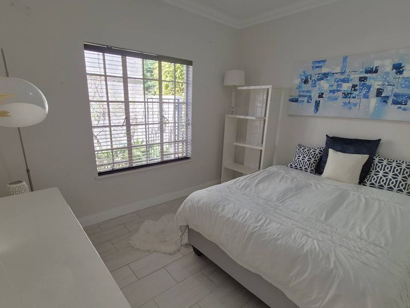 A bright and well-maintained bedroom featuring neutral tiled flooring, crown molding, and a window fitted with security bars and venetian blinds.