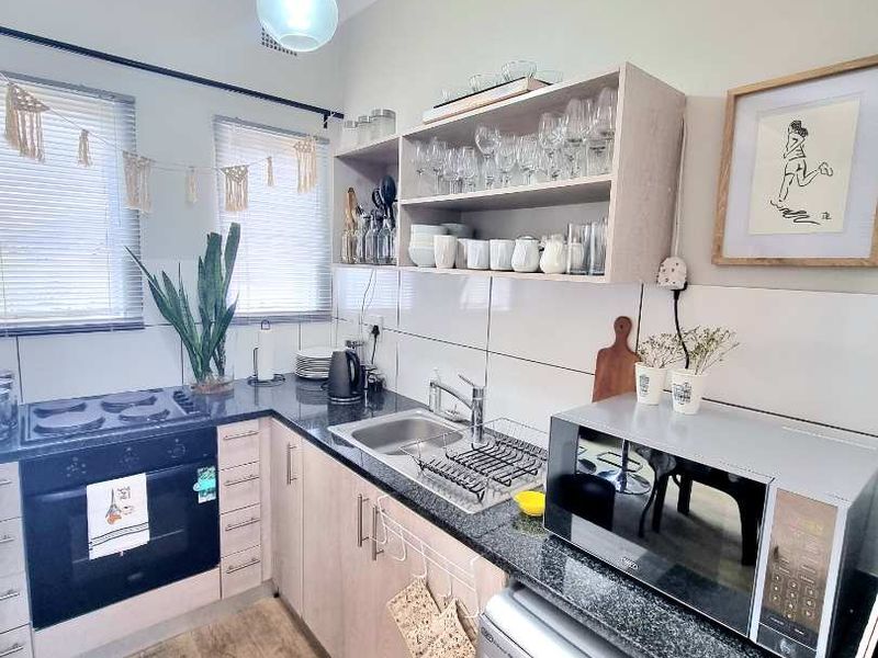 Compact kitchen featuring granite countertops, built-in oven, gas hob, stainless steel sink, and light wood cabinetry with open shelving.
