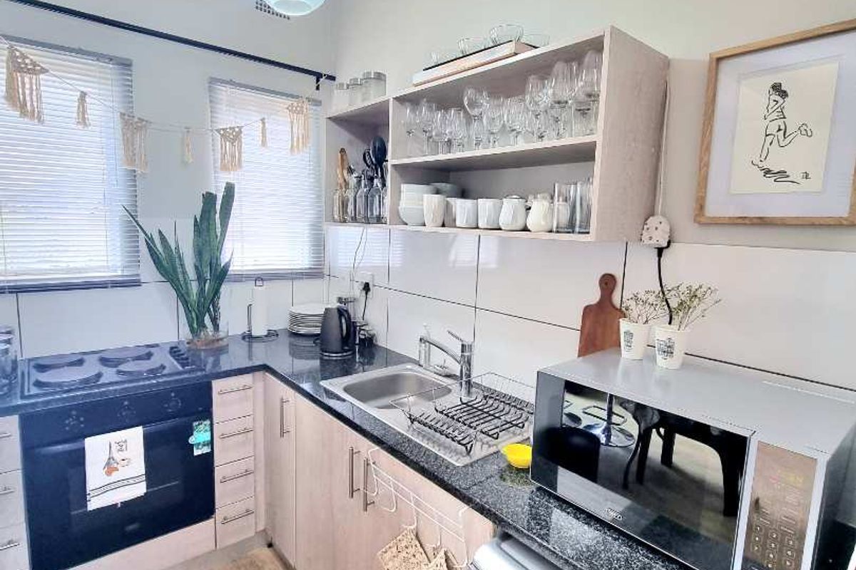 Compact kitchen featuring granite countertops, built-in oven, gas hob, stainless steel sink, and light wood cabinetry with open shelving.
