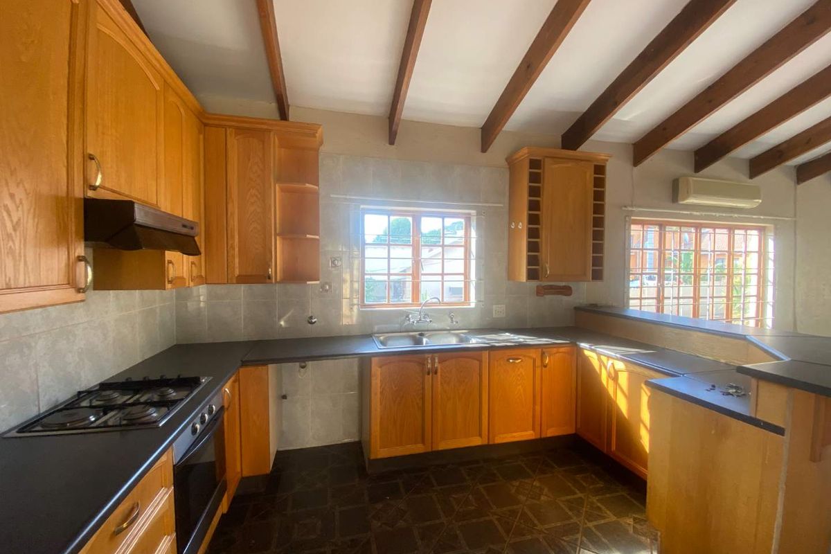 A functional kitchen featuring timber cabinetry, dark countertops, a built-in gas hob and oven, and exposed timber ceiling beams.