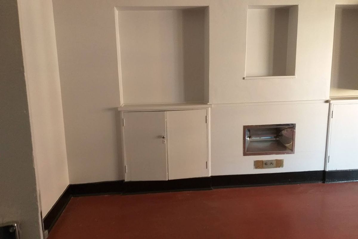 An empty living area featuring built-in cabinetry, wall niches, and a recessed wall heater, offering a blank canvas for renovation.
