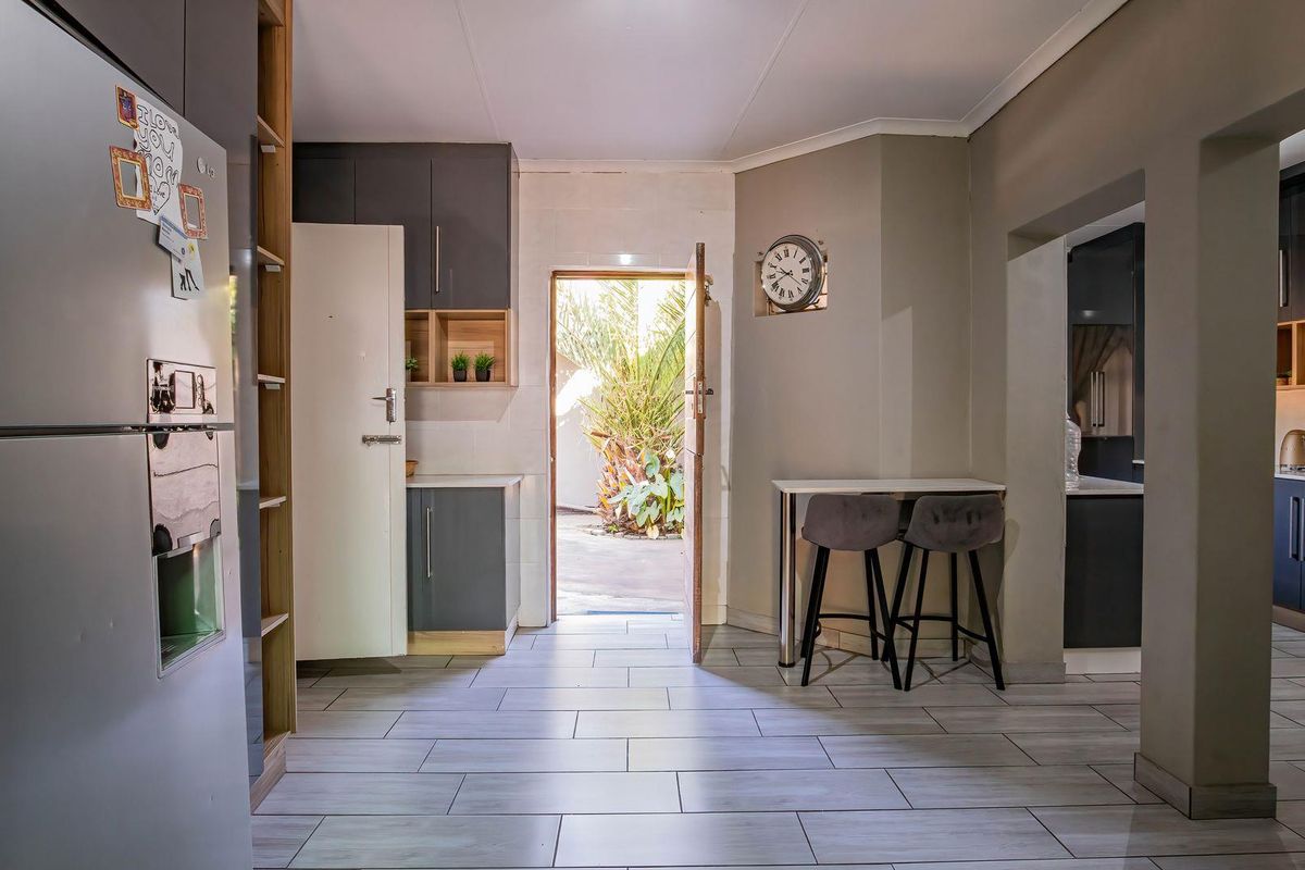 Modern kitchen area featuring contemporary grey cabinetry, open shelving, and tiled flooring, with direct access to the outdoor space.