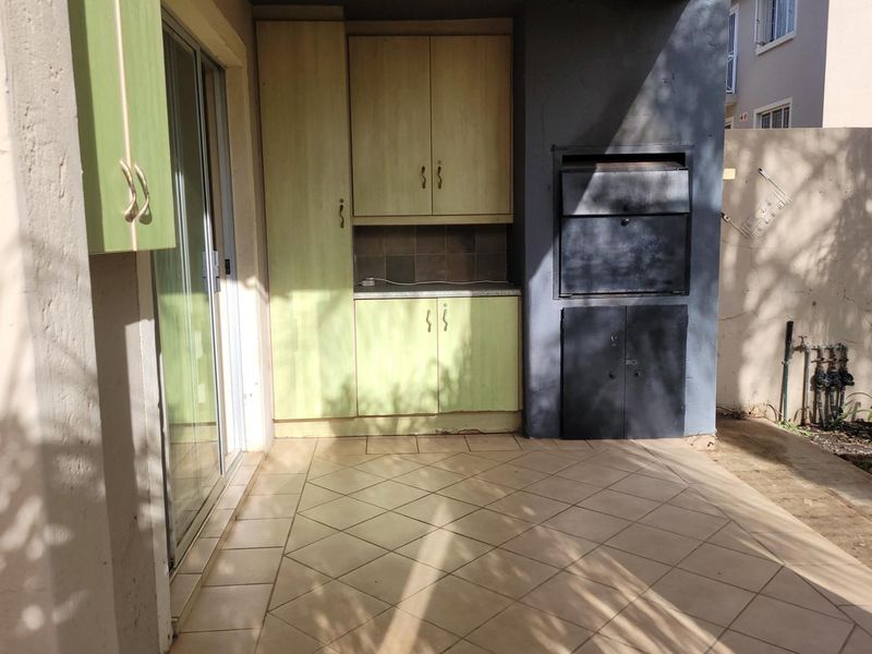 Covered patio area featuring a built-in braai, tiled flooring, and integrated storage cabinetry, providing a functional outdoor entertainment space.