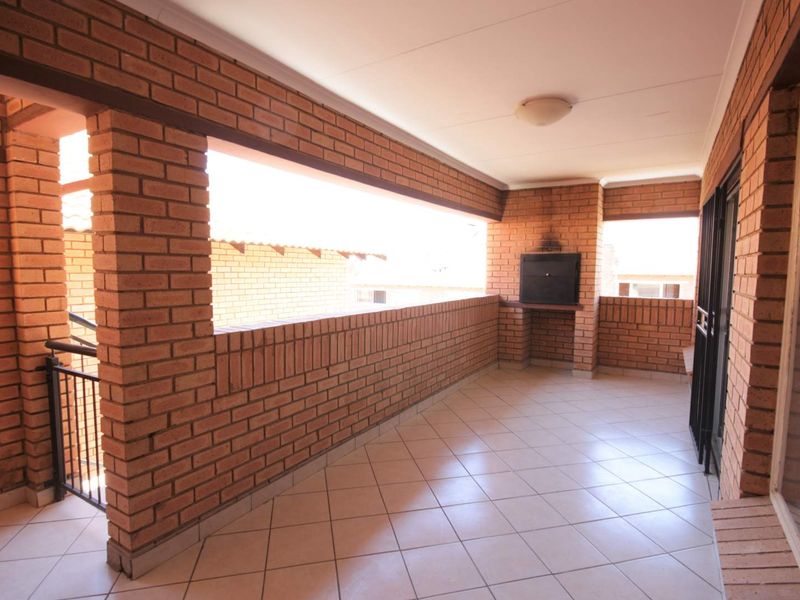 A spacious covered balcony featuring exposed brick walls, tiled flooring, and a built-in braai, offering a functional outdoor entertainment area.