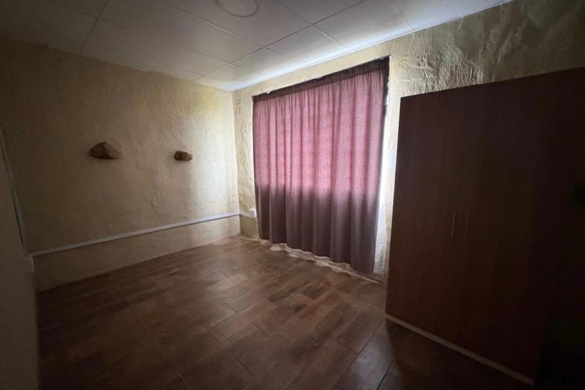 A simple bedroom featuring tiled flooring, textured walls, and a drop ceiling, providing a functional space with basic finishes.