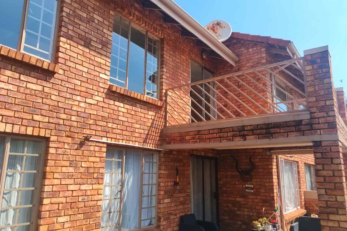 Rear elevation of a double-story face brick townhouse featuring an upper-level balcony with metal balustrade and ground-floor access via sliding glass doors.