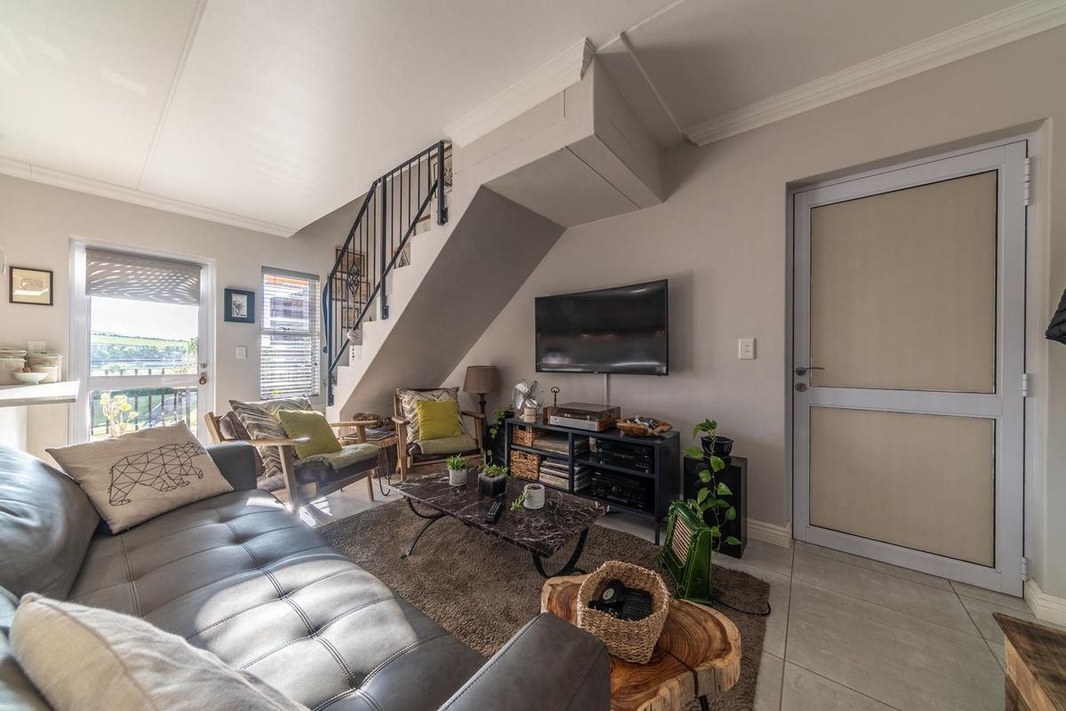 A well-maintained living room featuring tiled floors, crown molding, and a staircase with a metal balustrade, providing a functional and comfortable living space.