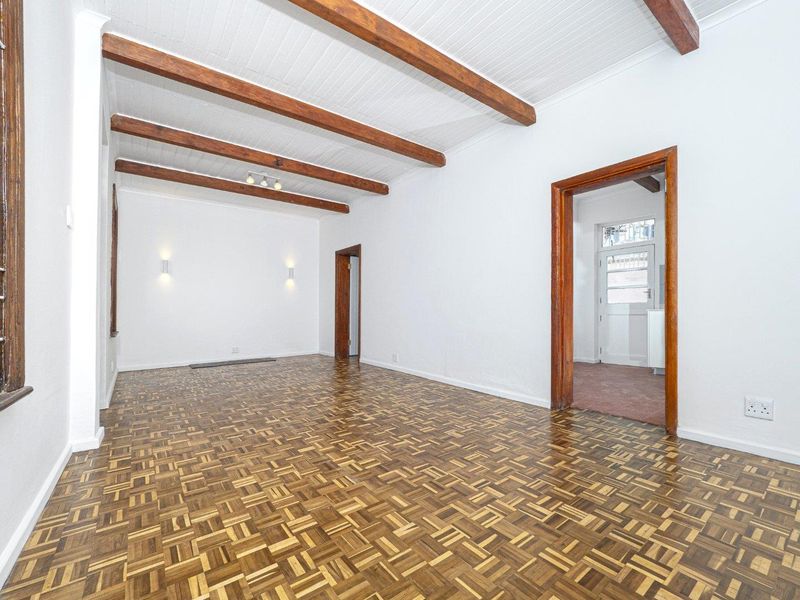 Spacious living area featuring classic parquet flooring, exposed timber ceiling beams, and neutral white walls, offering a bright and versatile living space.