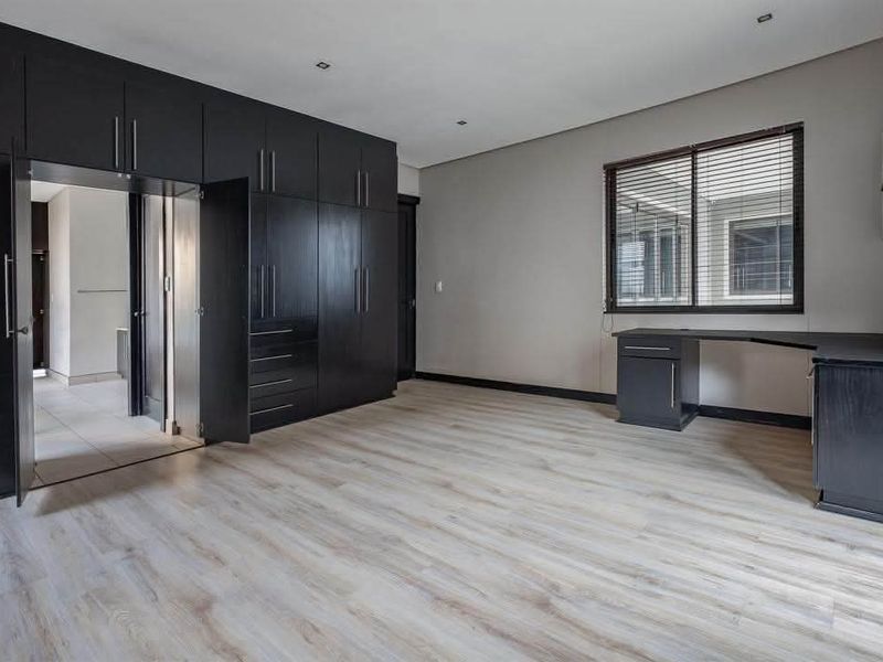 Spacious bedroom featuring extensive dark wood built-in cabinetry, a matching integrated desk, light laminate flooring, and recessed lighting.