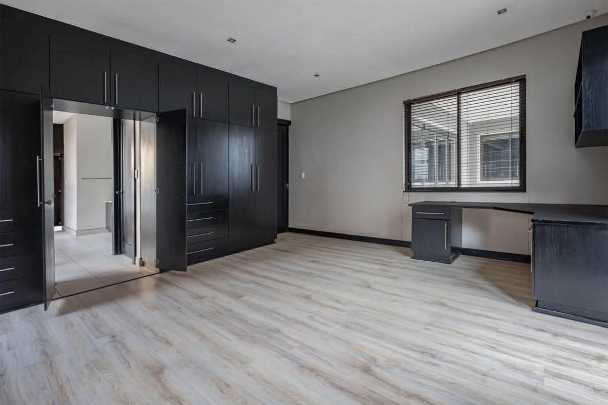 Spacious bedroom featuring extensive dark wood built-in cabinetry, a matching integrated desk, light laminate flooring, and recessed lighting.