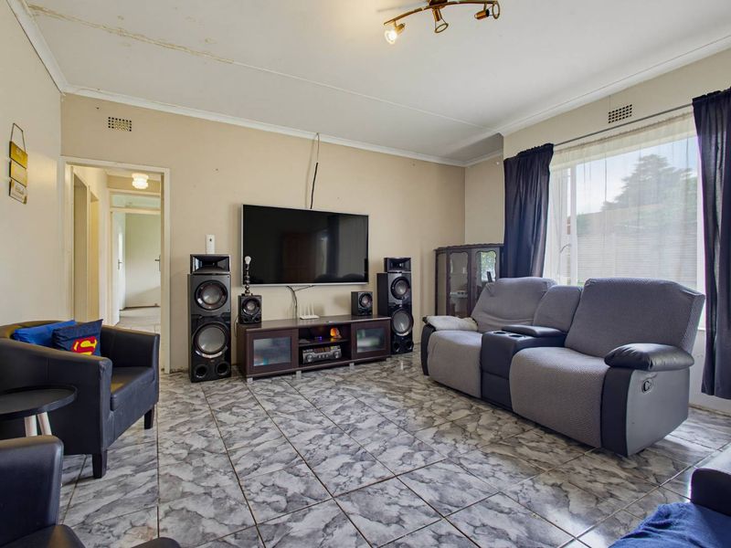 A living room featuring tiled flooring and a large window, currently showing signs of ceiling water damage and wear.
