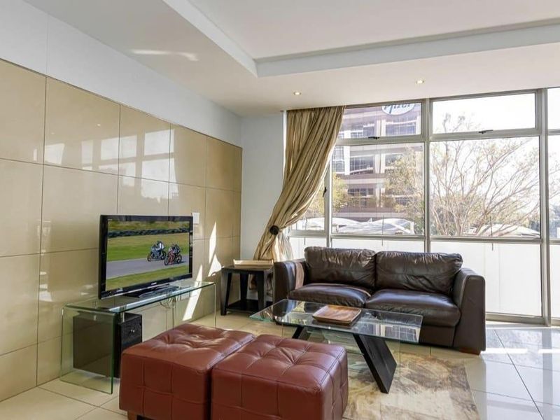 A bright living room featuring large floor-to-ceiling windows, tiled flooring, and a modern feature wall, offering ample natural light and a contemporary feel.