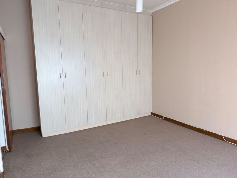A clean, empty bedroom featuring neutral wall tones, carpeted flooring, and extensive built-in cupboard storage.