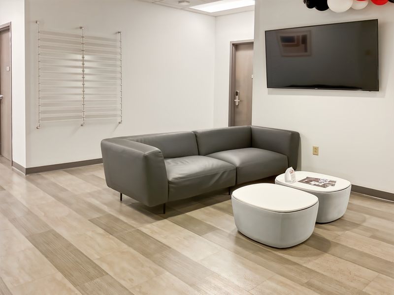 A modern office waiting area featuring wood-look flooring, recessed lighting, and a wall-mounted television.