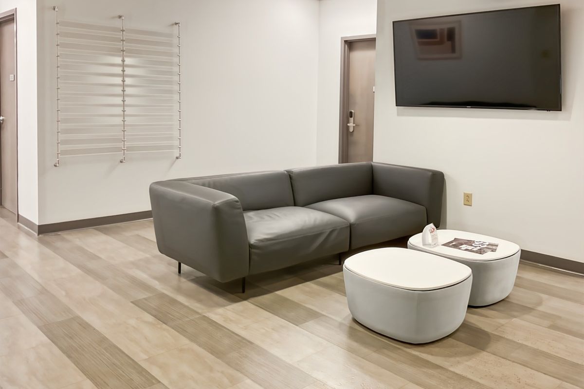 A modern office waiting area featuring wood-look flooring, recessed lighting, and a wall-mounted television.