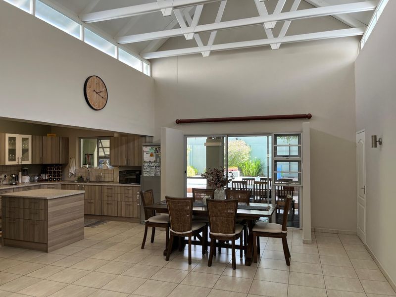 Spacious open-plan living and kitchen area featuring high vaulted ceilings with exposed trusses, tiled floors, and large sliding doors leading to the patio.